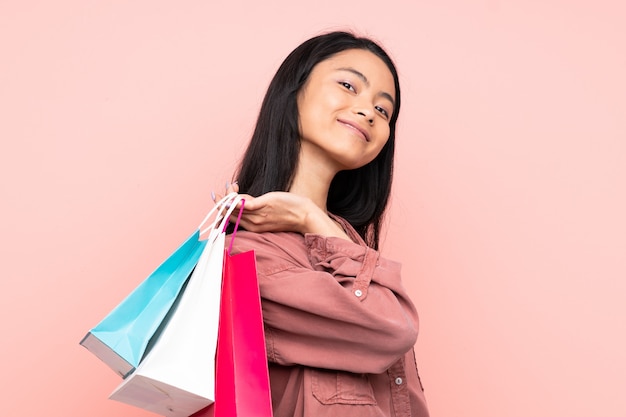 Adolescente fille chinoise isolée sur fond rose tenant des sacs à provisions et souriant