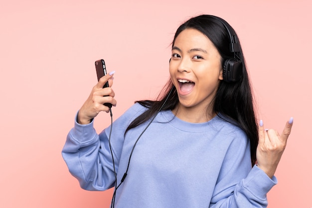 Adolescente fille chinoise sur mur rose écouter de la musique faisant un geste rock