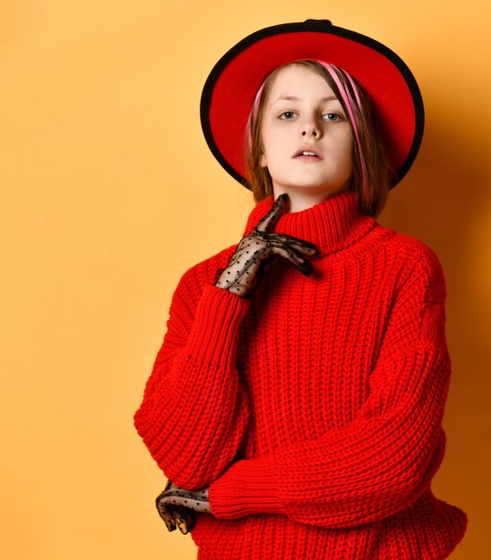 Adolescente fille dans un chapeau fedora et un pull rouge vif, elle est sur un fond de studio jaune