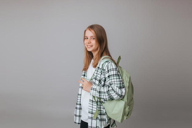 Adolescente Gaie De 111213 Ans Dans Un Uniforme Scolaire Porte Un Sac à Dos Sur Un Fond Gris Mode Scolaire