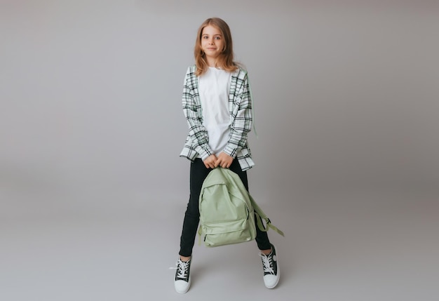 Photo adolescente gaie de 111213 ans dans un uniforme scolaire porte un sac à dos sur un fond gris mode scolaire