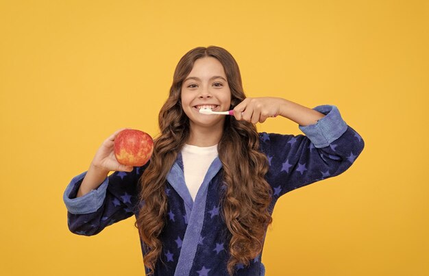 Adolescente gaie aux cheveux bouclés en pyjama confortable se brosser les dents et tenir la dentisterie aux pommes