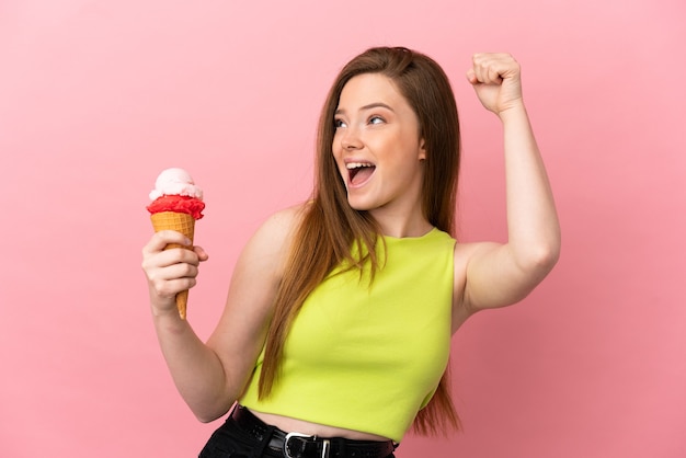 Adolescente avec une glace au cornet sur fond rose isolé célébrant une victoire