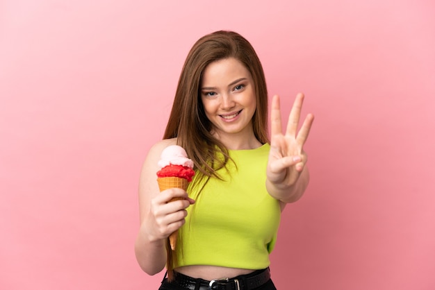 Adolescente avec une glace au cornet sur fond rose isolé heureux et comptant trois avec les doigts