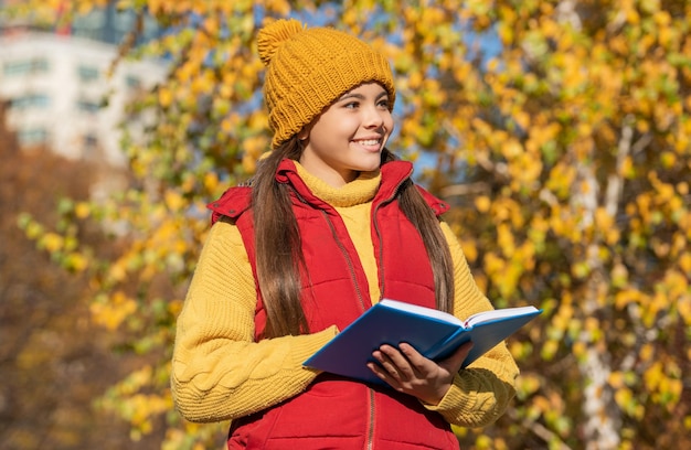 Une adolescente heureuse a lu un livre scolaire en automne