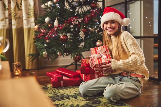 Adolescente heureuse s'asseyant à l'arbre de Noël