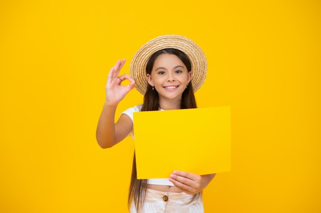 Une adolescente heureuse tient du papier publicitaire vide avec un espace de copie sur fond jaune ok