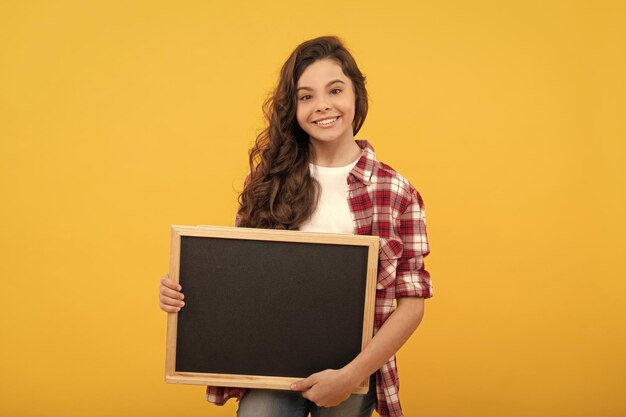 Une adolescente heureuse tient le tableau noir de l'école pour la promotion de l'espace de copie