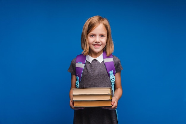 Une adolescente heureuse en uniforme scolaire tient une pile de livres Bannière d'une écolière Portrait d'une écolière avec un espace pour copier sur un fond bleu