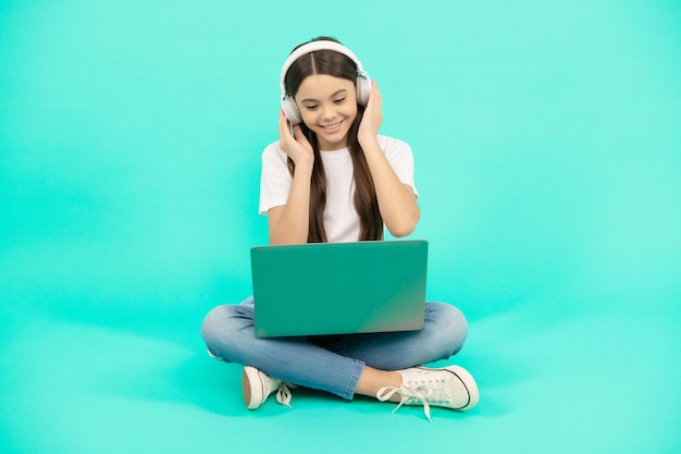 une adolescente heureuse utilise un ordinateur sans fil pour un appel vidéo ou écoute un webinaire dans un casque, une formation en ligne.