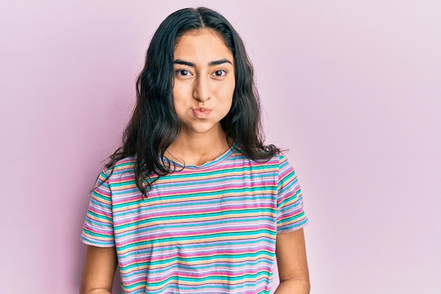 Adolescente hispanique avec des appareils dentaires portant des vêtements décontractés gonflant les joues avec un drôle de visage. bouche gonflée d'air, expression folle.