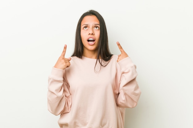 Adolescente hispanique mignonne jeune femme pointant vers le haut avec la bouche ouverte.