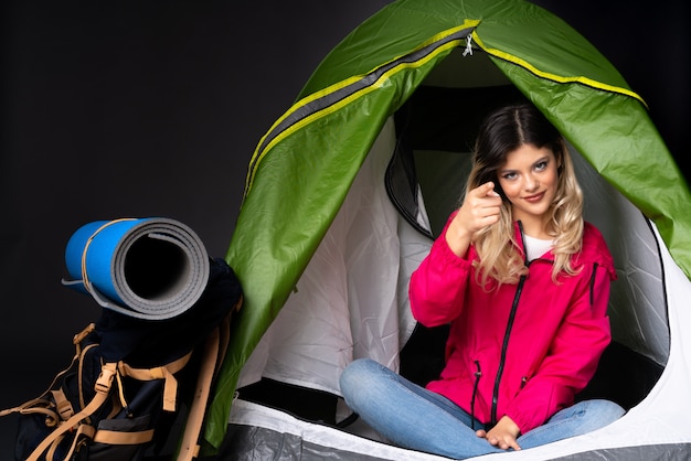Photo adolescente à l'intérieur d'une tente de camping verte sur un mur noir montrant et levant un doigt
