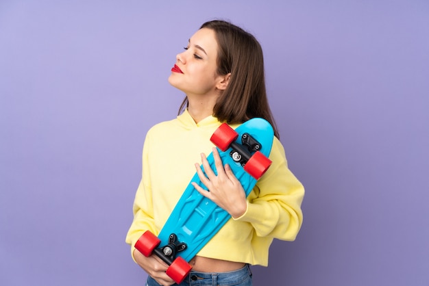 Adolescente isolée sur mur violet avec un patin avec une expression heureuse