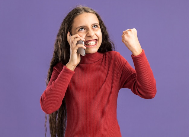 Adolescente joyeuse parlant au téléphone en levant en train de faire un geste oui isolé sur un mur violet