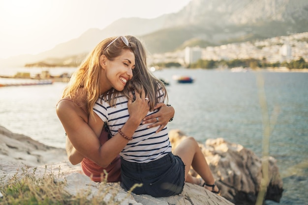 Une adolescente joyeuse et sa jeune maman dans une étreinte profitent de vacances d'été sur une plage de rochers marins.