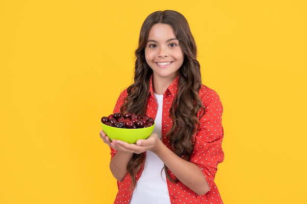 Une adolescente joyeuse tient un bol de cerises sur fond jaune