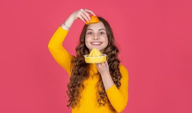 Une adolescente joyeuse tient une orange et un presse-agrumes sur fond rose