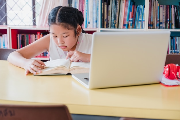 Adolescente, lecture de livre avec ordinateur portable dans la bibliothèque. Concept de l&#39;éducation et de l&#39;alphabétisation