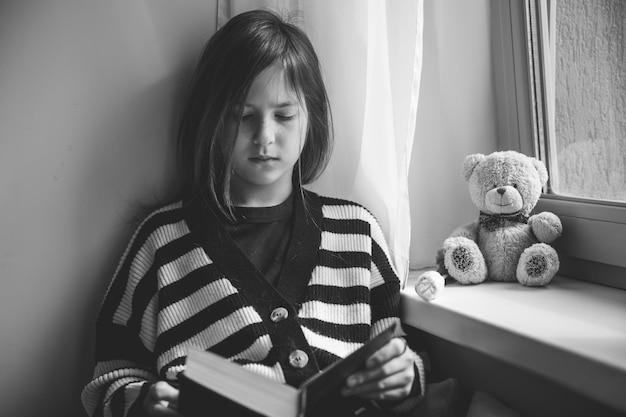 Photo adolescente lisant un livre à la maison près de la fenêtre