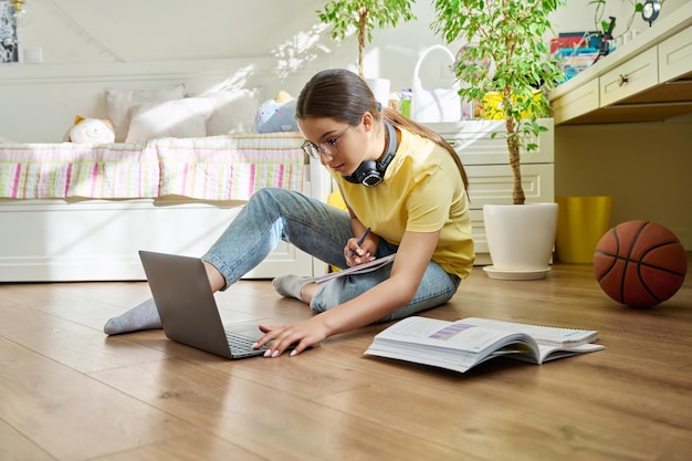 Une adolescente avec des lunettes qui étudie à la maison avec un ordinateur portable