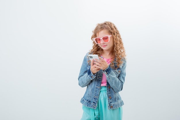 Une adolescente à lunettes de soleil tenant un téléphone montre une surprise sur un fond blanc