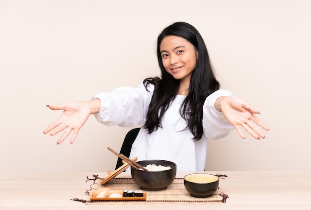 Adolescente, manger de la nourriture asiatique isolée sur beige présentant et invitant à venir avec la main