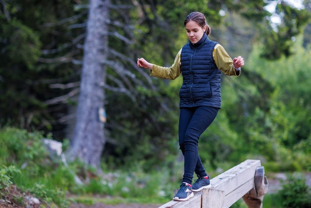 Une adolescente marche le long d'une bûche inclinée et passe un parcours d'obstacles forestiers dans une forêt de pins