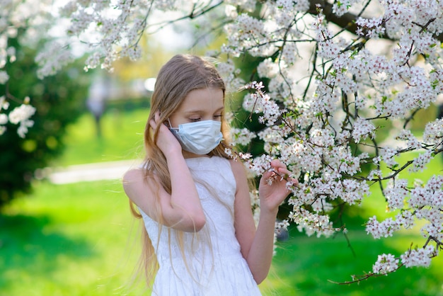 Adolescente en masque médical dans le jardin fleuri de printemps. Concept de distance sociale et prévention du coronavirus.