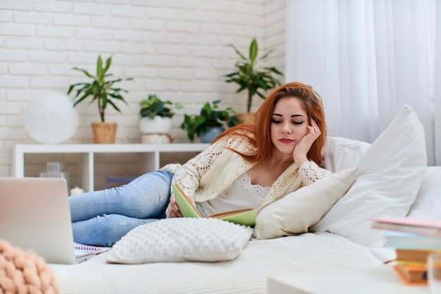 Adolescente mignonne fait ses devoirs allongé sur le lit à la maison. Apprentissage à distance.