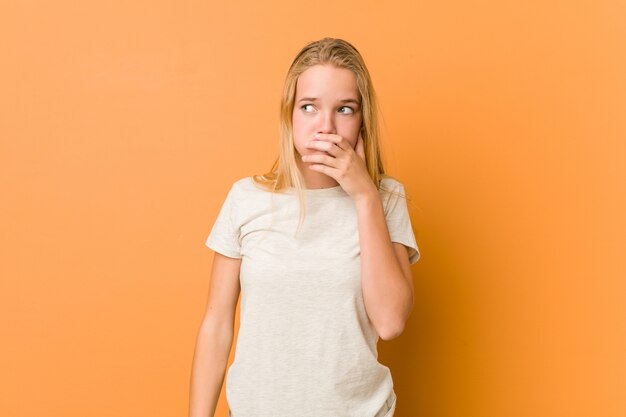 Adolescente mignonne et naturelle réfléchie à la recherche d'un espace copie couvrant la bouche avec la main.