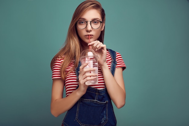 Adolescente mignonne en salopette en jean et lunettes avec soda