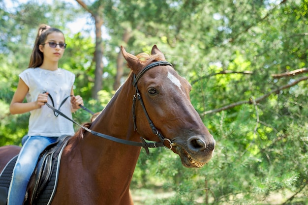 Adolescente montant un cheval brun, équitation pour les personnes dans le parc.