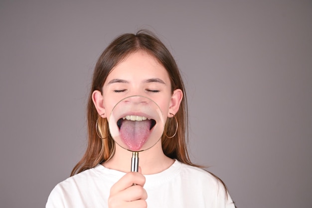 Adolescente montre la langue à travers la loupe Fille montrant sa langue isolée sur fond gris Émotions