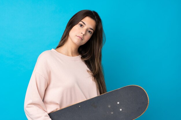 Adolescente sur mur bleu isolé avec un patin