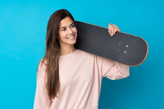 Adolescente sur mur bleu isolé avec un patin