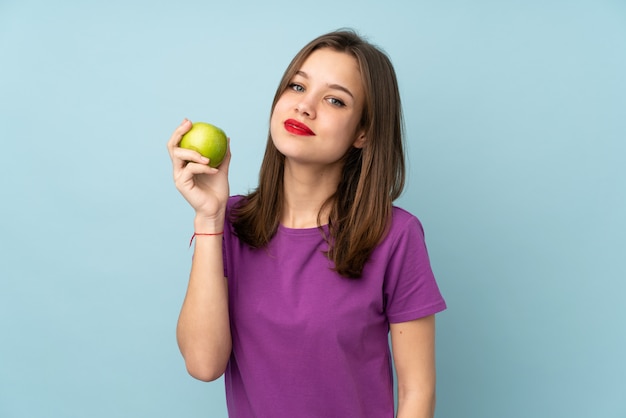 Adolescente sur mur bleu avec une pomme et heureux