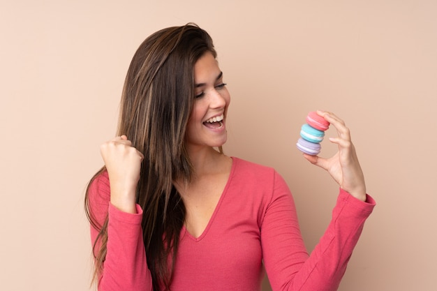 Adolescente sur mur isolé tenant des macarons français colorés et célébrant une victoire