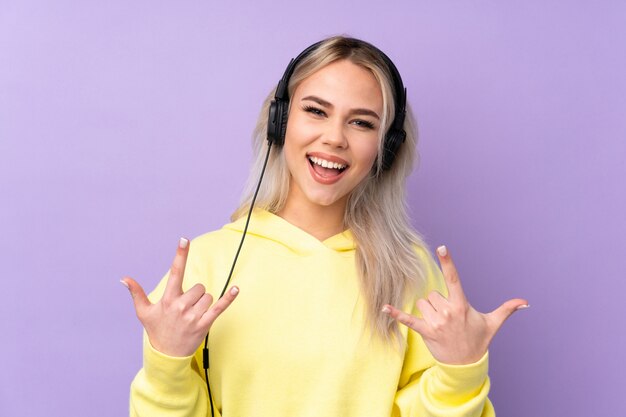 Adolescente sur mur violet écouter de la musique faisant un geste rock