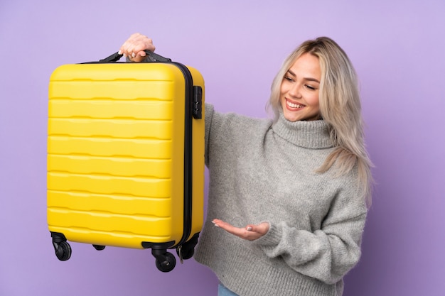 Adolescente sur mur violet isolé en vacances avec valise de voyage