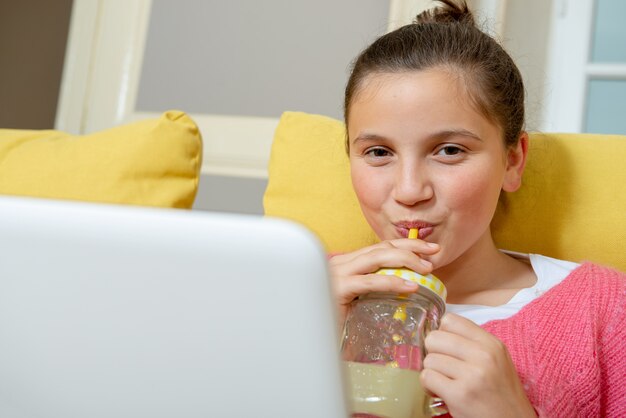 Adolescente avec un ordinateur portable buvant un jus d&#39;orange