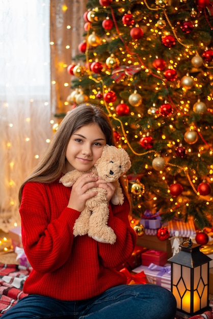 Adolescente avec ours en peluche près de l'arbre de Noël Enfant avec son cadeau près de l'arbre de Noël décoré