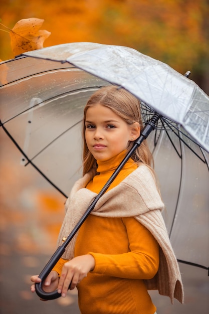 une adolescente avec un parapluie transparent dans les mains lors d'une promenade en automne dans une rue de la ville