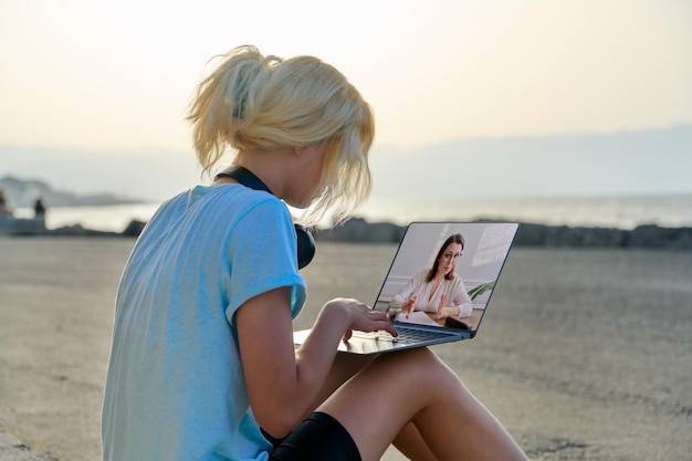 Adolescente parlant en ligne avec un thérapeute utilisant un ordinateur portable en plein air au bord de la mer