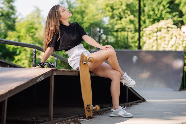 Adolescente patineuse avec une planche à roulettes assise dans le parc des patineurs