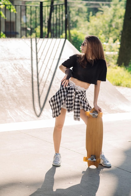 Adolescente patineuse tenant une planche à roulettes debout dans le parc des patineurs