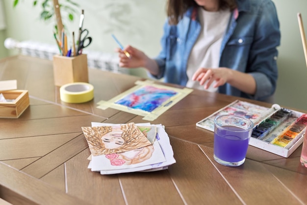 Adolescente peignant à l'aquarelle, assise à la maison à la table. Art, éducation, créativité, loisirs des adolescents