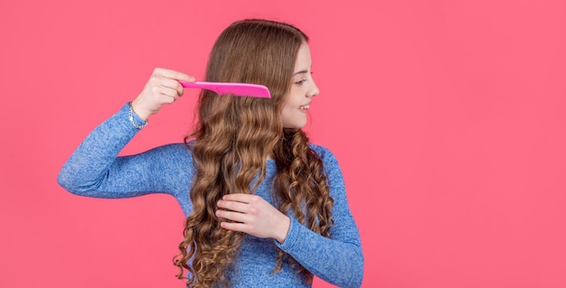 Adolescente peignant les cheveux bouclés avec une brosse à cheveux sur l'espace de copie de fond rose