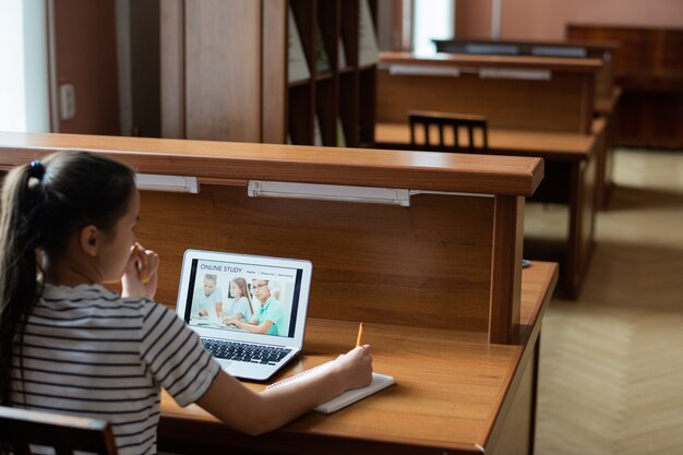 Adolescente Pensive Assis Par 24 En Face De L'écran De L'ordinateur Portable Avec Page D'accueil Du Site Web D'apprentissage à Distance