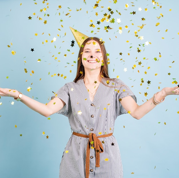 Adolescente portant chapeau d'anniversaire doré jetant des confettis